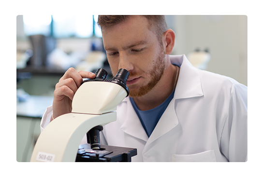 homem com jaleco branco olhando o microscópio